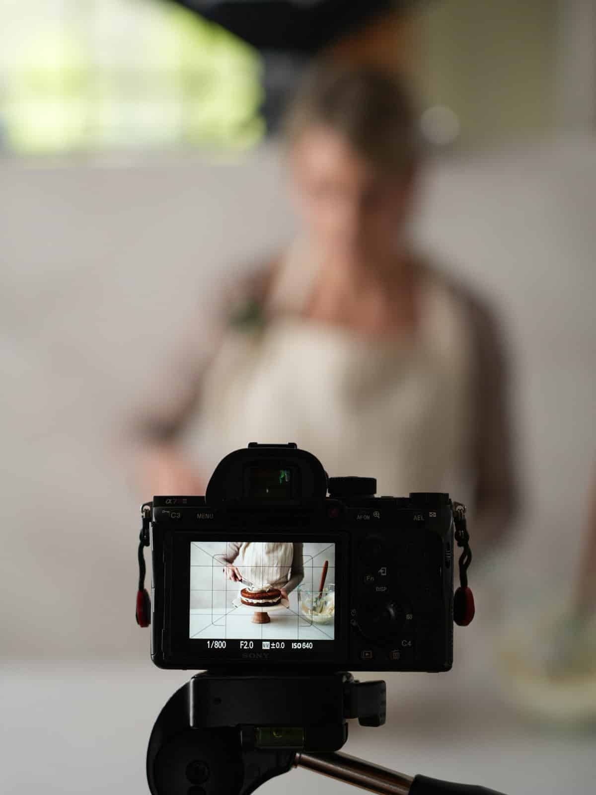 camera showing Sally spreading frosting on layer cake.