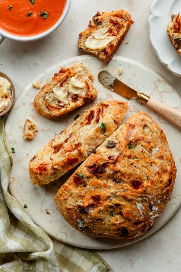 crusty bread sliced and sitting on marble circle with bowls of tomato soup.