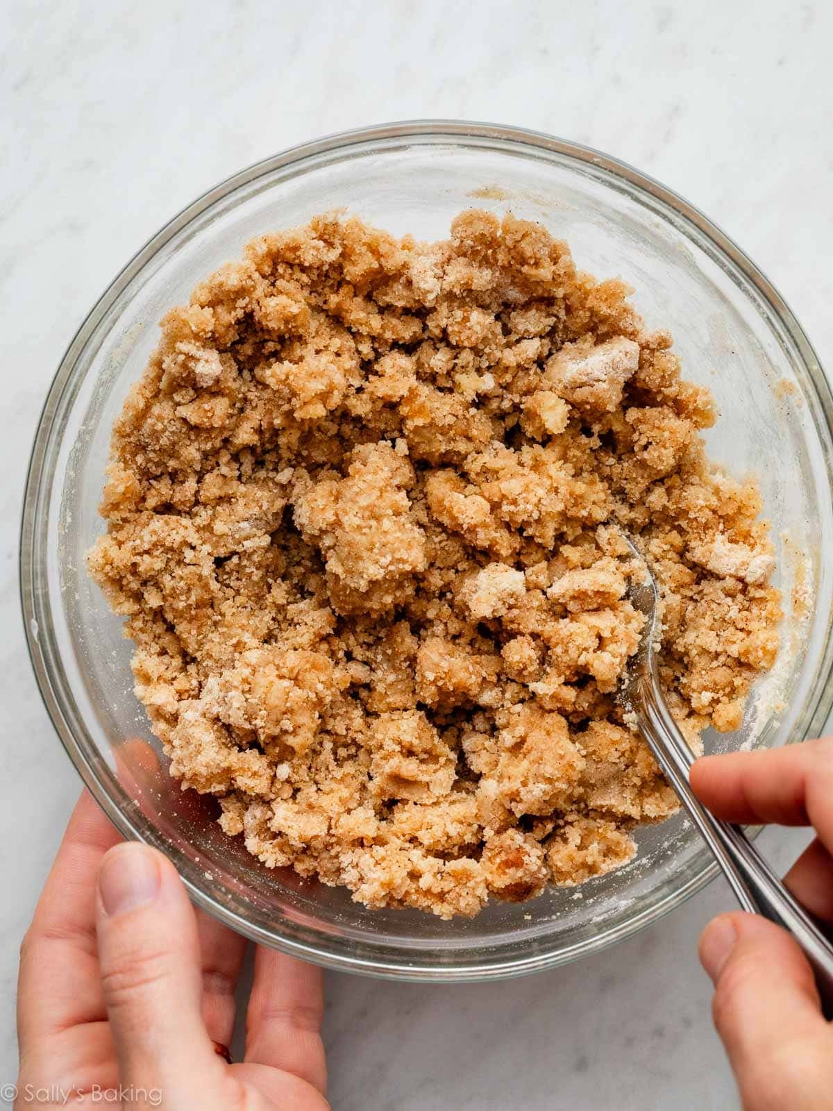 hands using a fork to stir crumbly ingredients.
