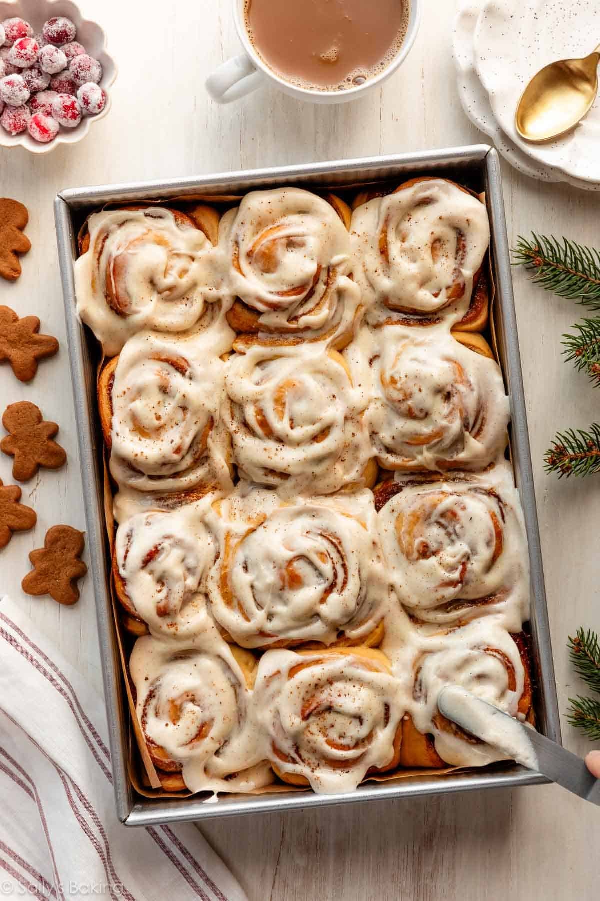 gingerbread cinnamon rolls in baking pan with sugared cranberries and mini gingerbread cookies next to it.