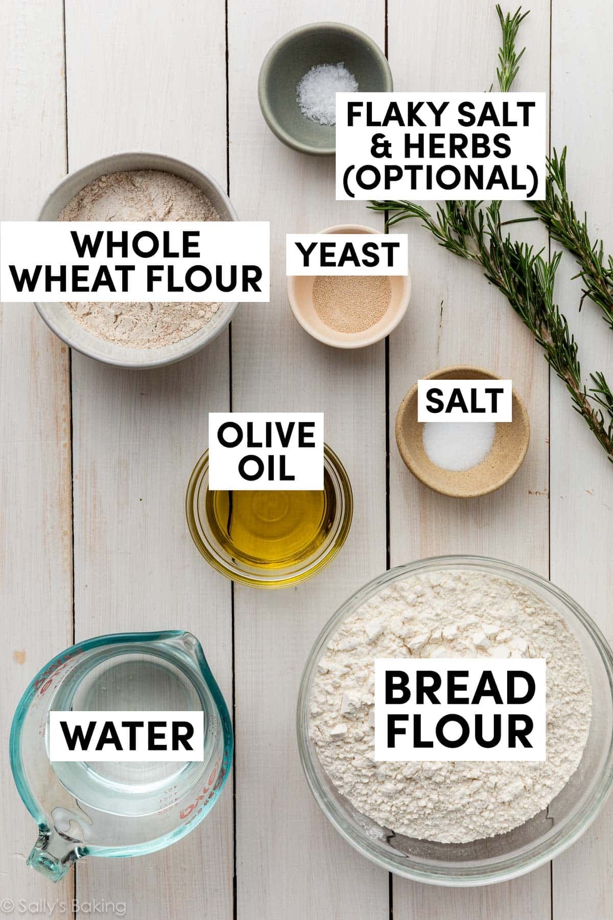 ingredients on wooden backdrop including water, flour, olive oil, salt, yeast, and rosemary.