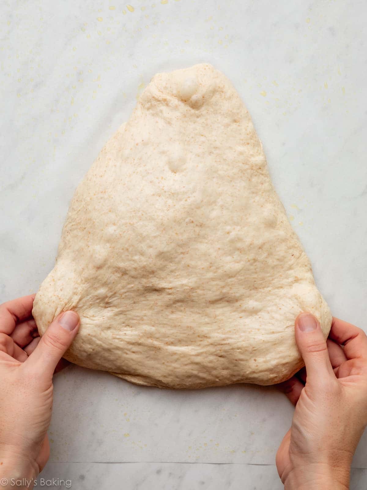hands stretching dough into rounded triangle shape.