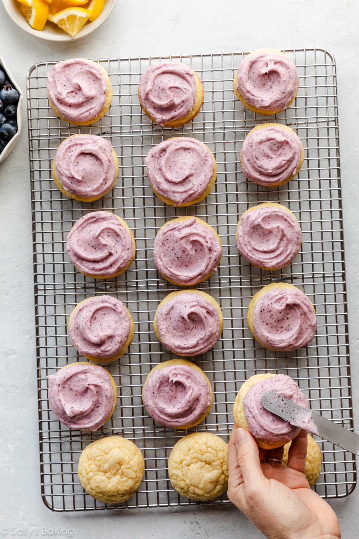 hand spreading blueberry frosting on cookies.